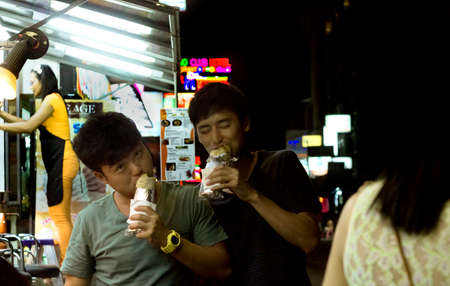 SOI SANSABI, PATONG BEACH, PHUKET, THAILAND, 16 SEPTEMBER 2013: Two Chinese tourists munch on a kebab wrap while out on the town in Patong Beach.のeditorial素材