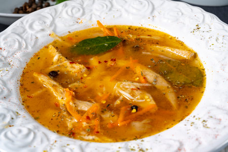 Chicken soup with vegetables and spices in a white plate on a black backgroundの写真素材