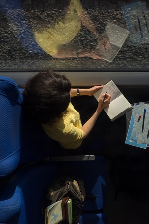 young woman loking in diary book and writing travel blog train during traveling in train near window