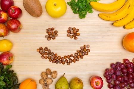 Flat lay of arranged hazelnuts in smile face surrounded with plenty of healthy fresh fruit and gree on wood.の写真素材