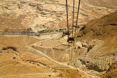 Cable car track, moving down from Masada fortress to Judean desert Israel. Ancient Roman fortifications are seen at the bottom of the mountain. Legendary Middle East places for touristsの写真素材