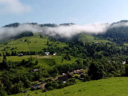 Flying over white clouds and little village in the mountains. Natural aerial view