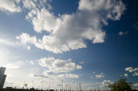 Deep blue summer sky with white fluffy clouds over city housesの写真素材