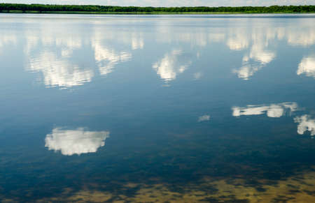 Deep blue summer sky with white clouds reflecting in pure lake water, water mirror natural...