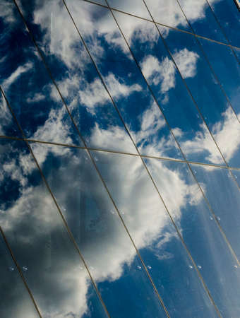 Reflection of clouds and blue sky in the glass wall of a modern business center, photo backgroundの写真素材
