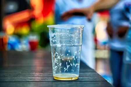 A glass of water on a wooden table with blurred people in the backgroundの写真素材