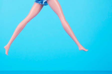Barefoot doll legs on blue background. Minimal happiness concept.の写真素材