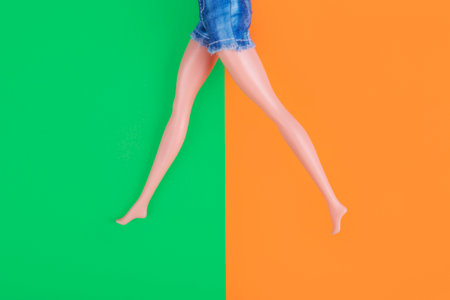 Barefoot doll legs on green and orange background. Minimal happiness concept.の写真素材