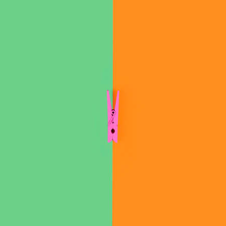 Pink laundry clip on green and orange background divided in halfの写真素材