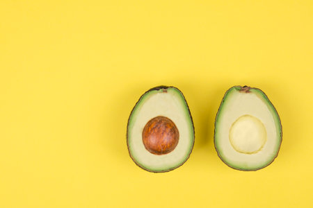Avocado cut in half on bright yellow background