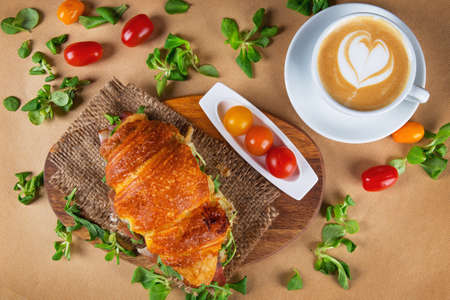 Croissant sandwich with cherry tomatoes and hot cappuccino coffee