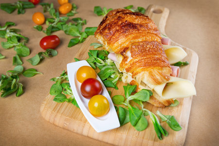Croissant sandwich filled with ham and cheese on wooden chopping boardの写真素材