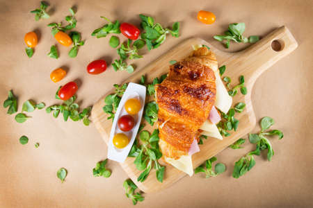 Croissant sandwich filled with ham and cheese on wooden chopping boardの写真素材