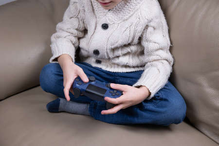 Child using technology. The boy sits on the couch, holds a game joystick and plays video games.