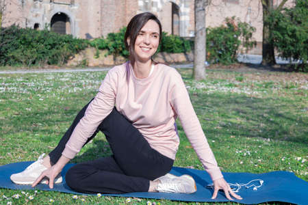 Young woman with long hair doing yoga on mat in the city park. Breathing practices and mental health.の写真素材