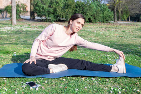 Young woman with long hair doing yoga on mat in the city park. Breathing practices and mental healthの写真素材