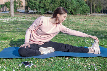 Young woman with long hair doing yoga on mat in the city park. Breathing practices and mental health