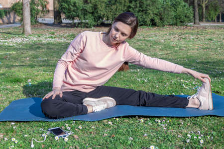 Young woman with long hair doing yoga on mat in the city park. Breathing practices and mental health.の写真素材