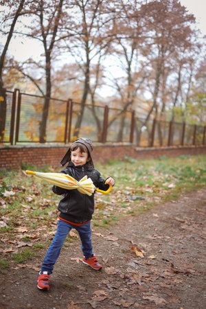 A six-year-old funny boy plays with a yellow umbrella in an autumn park. Childrens fantasy conceptの写真素材