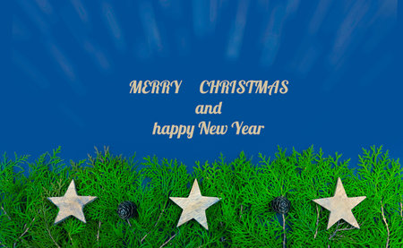 Flat lay Christmas card on blu background with Thuja branches and wooden stars, with sample text.の写真素材