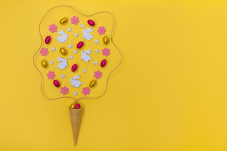Ice cream waffle horn with Easter decoration wooden flowers, rabbits and eggs on yellow background.の写真素材