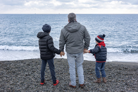 Man and two boys from behind and hold hands on the beach and look at the sea. Happy fathers dayの写真素材