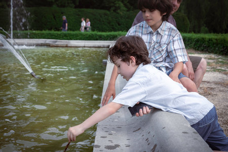 Two brothers are sitting in a summer park near a fountain and playing in the water. Family have fun.の写真素材