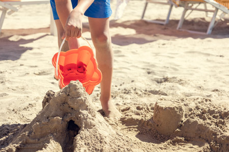 Close-up of childrens hands pouring water from bucket to play with sand and build castle on beach.の写真素材