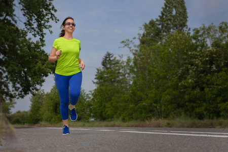 Young hispanic woman running on path during cardio workout on sunny summer day in city park.