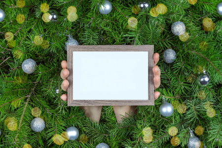 Female hands holding a frame against a Christmas branches with silver ballsの写真素材