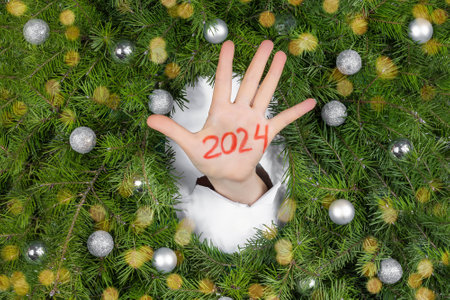 Female hand with number 2024 against Christmas branches with silver balls and bokeh.の写真素材