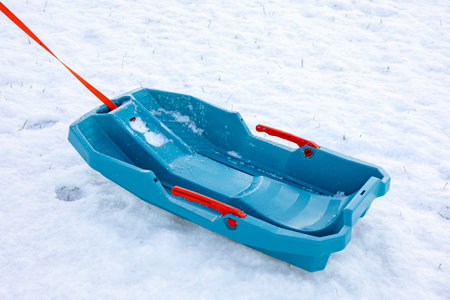 Empty blue plastic sled with a red rope lies on a snow-covered ground.Concept representing winter sports, childhood, leisure activities during the cold season, and family fun.Space for textの写真素材
