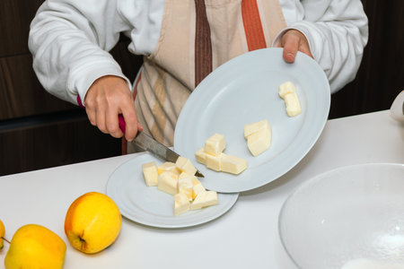 Close-up of female hand preparing butter in kitchen with knife and apples nearby. Stage of cooking pie.の写真素材