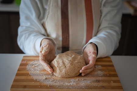 Close up hands of woman preparing whole wheat dough on wooden board with flourの写真素材