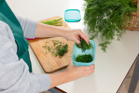 Woman storing freshly chopped dill in container for preserving herbs. Preparing dill for winter...