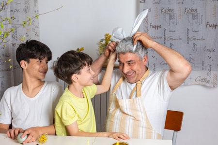 Happy father having fun with his kids while wearing bunny ears headband. Joyful Easter moments, spring family celebration, playful bonding time at homeの写真素材