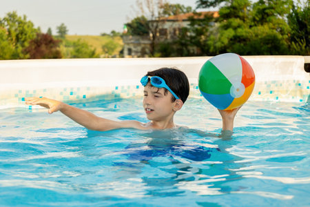 Boy playing with colorful beach ball in an outdoor pool on a sunny summer day, enjoying water fun...