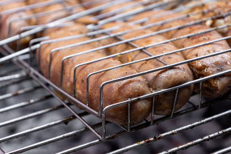 Close up juicy sausages grilling in a metal basket over hot coals, filling the air with mouthwatering aromas and creating an irresistible barbecue atmosphere perfect for summer gatheringsの写真素材