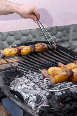 Hands of chef grilling skewers of potatoes and bacon over hot coals on an outdoor barbecue grill, creating a smoky and flavorful meal perfect for summer picnics and gatheringsの写真素材