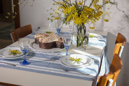 Dining table decorated for an easter celebration featuring a traditional colomba cake, mimosa...