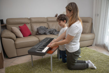 Mother guides her sons hands on a keyboard, teaching music and building warm family bonding in a...