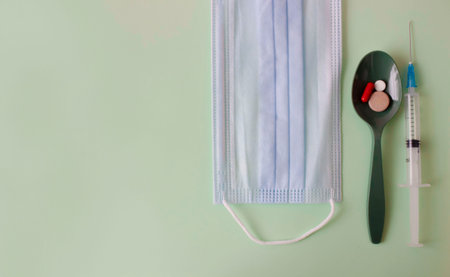 A green spoon with tablets, a medical mask and a syringe on a colored background. Medical layout