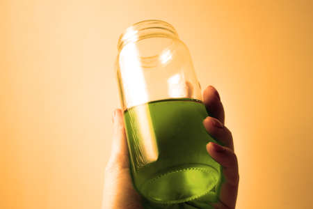 Glass jar with green liquid in a female hand on a orange backgroundの写真素材