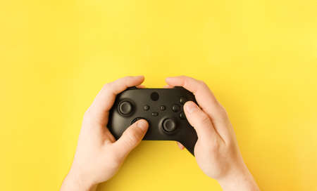 Close-up of a man holding a gamepad and play video games on a yellow background. Place for your text.の写真素材