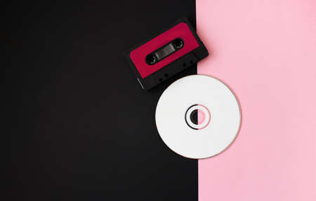 Black audio cassette and white disc on pink-black background. 80s. Top View. Flat lay.の写真素材