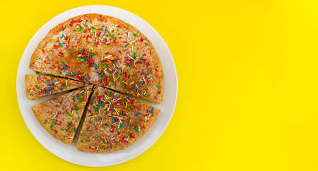 flat cake with colored sprinkles on yellow background, top view.
