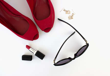 Red shoes, red lipstick, sunglasses and earrings on a white background. Beauty blog concept. Flat...