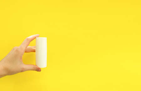 Female hand holding white cosmetic bottle on yellow background. Mock up, copy space. Summer skincare...