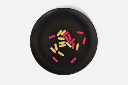 yellow and pink capsules on a black plate on a white backgroundの写真素材
