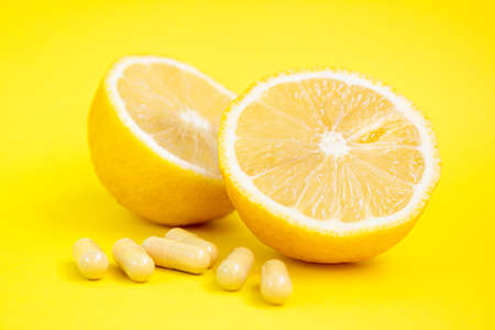 Vitamin capsules. Vitamin C pills and yellow lemon on yellow background.